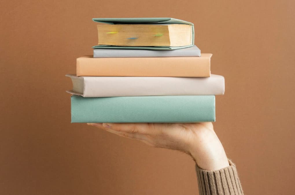 Arm holding a stack of books against a brown backdrop