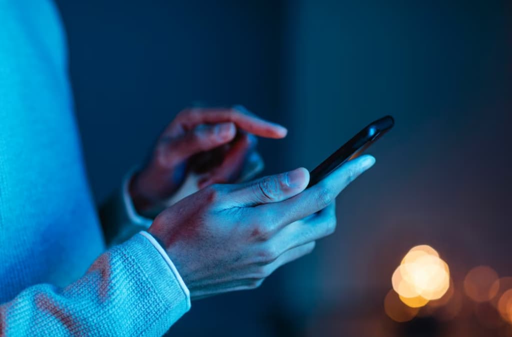 Close-up of hands using a smartphone with a glowing blue light in the background